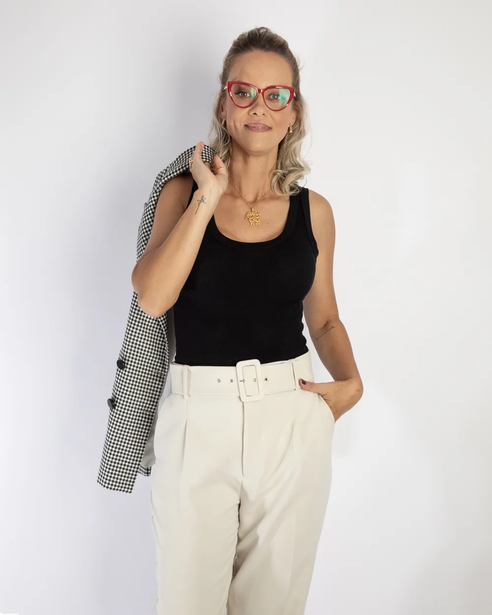 Carol Basilio de óculos vermelhos, regata preta e blazer xadrez no ombro